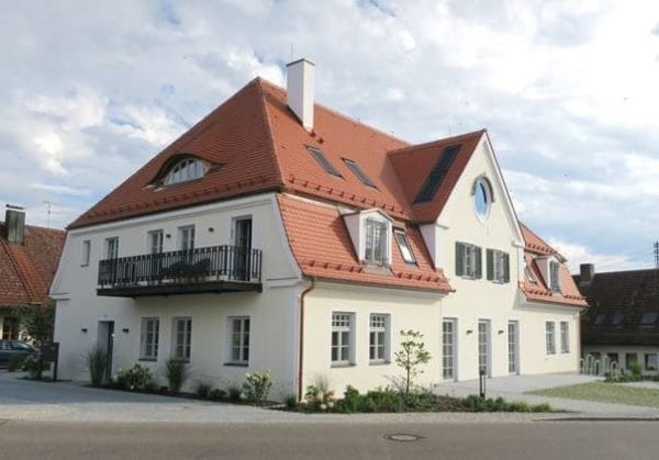 Außenansicht eines modernen Mehrfamilienhauses mit rotem Satteldach, Balkonen und saniertem Fassadenkonzept.