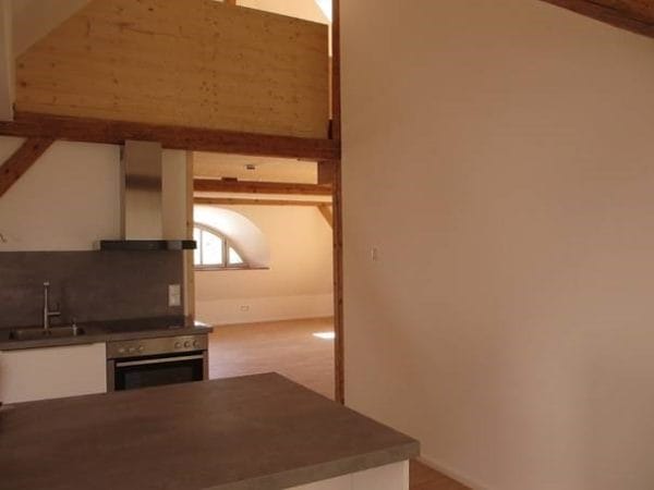 Offene Wohnküche mit Holzbalken, Kochbereich und Blick in einen großen, hellen Wohnraum