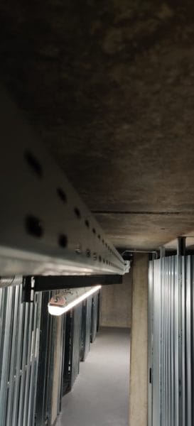 Kabeltrasse mit sauber geführten Leitungen und Feuchtraum-LED-Leuchte über Abteilen im Keller, installiert von SHI Gebäudetechnik.