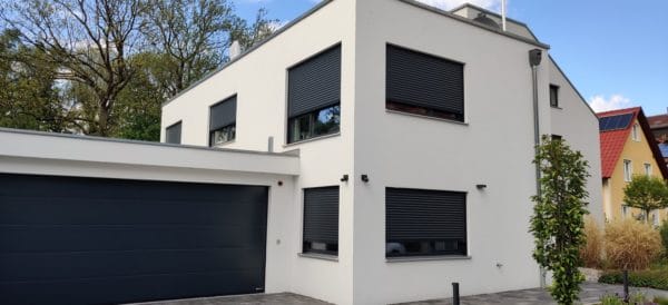 Außenansicht eines modernen Einfamilienhauses in Dachau mit grauer Putzfassade, Fenstern mit Rollläden