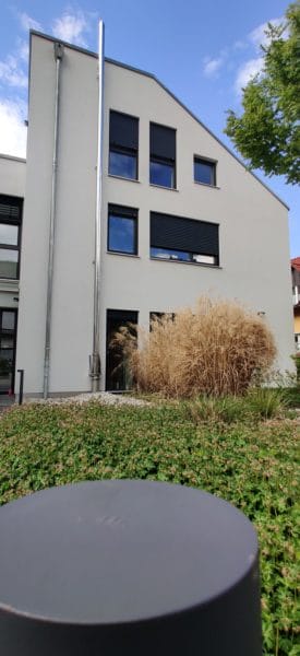 Außenansicht eines modernen Einfamilienhauses in Dachau mit grauer Putzfassade, Fenstern mit Rollläden und Garten-Pollerleuchte im Vordergrund