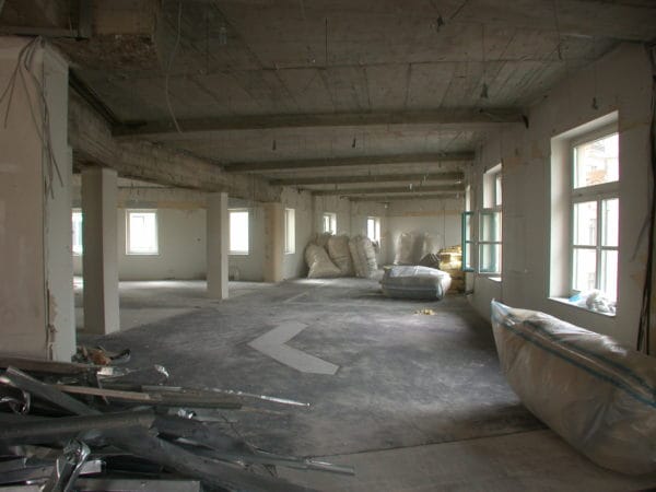 Elektro- und Sanitärinstallation im Rohbau: Kabelbündel, rote Brandschutz-/Leitung und Siphon an geöffneter Wand