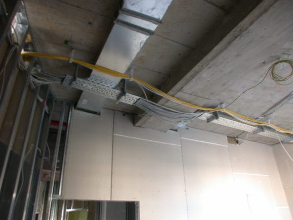 Kabeltrassen mit gelben und grauen Leitungen unter Betondecke neben Lüftungskanal im Praxisumbau