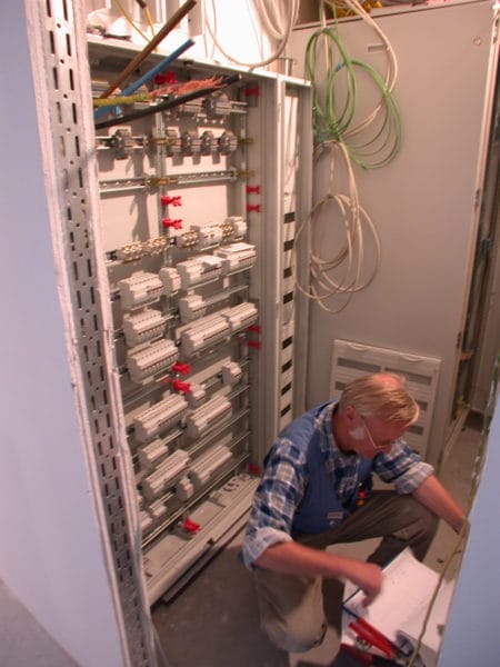 Elektriker prüft geöffnete Elektroverteilung mit Hutschienen in Arztpraxis