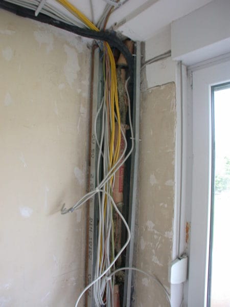 Offener Leitungsschacht mit gelben und weißen Kabeln neben Fenster – Elektroinstallation