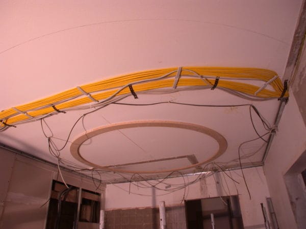 Offene Deckeninstallation mit gelben Kabelbündeln und rundem Deckenausschnitt im Praxisumbau von Dr. Naumann – SHI Elektro & Licht