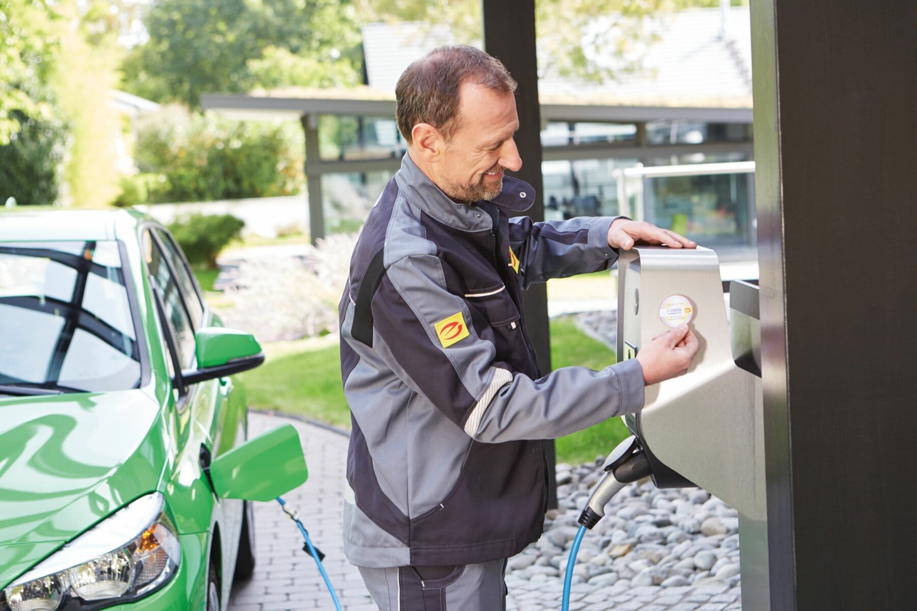 Elektrofachmann klebt E-CHECK E-Mobilität Plakette an Ladestation