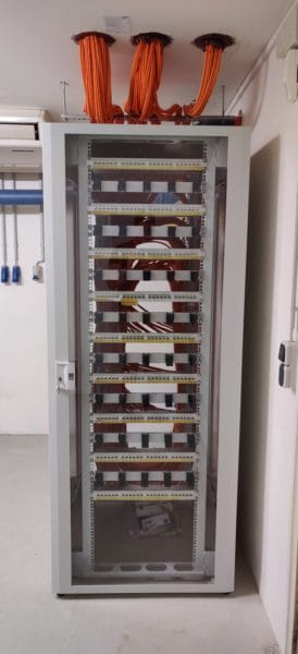 Netzwerkschrank mit vielen sortierten, roten Kabeln und Glastür