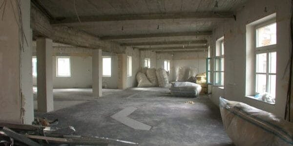 Elektro- und Sanitärinstallation im Rohbau: Kabelbündel, rote Brandschutz-/Leitung und Siphon an geöffneter Wand